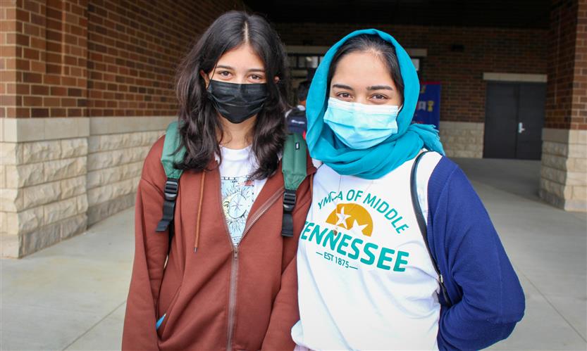 Two students stand in front of a middle school while wearing masks